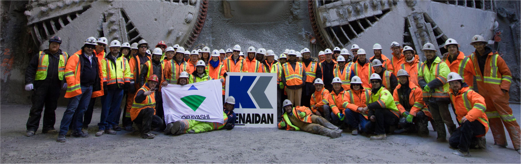 A group of Kenaidan employees standing in front of heavy machinery 